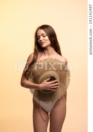 Young woman enjoying summer vibes, wearing swimwear and covering herself with a straw hat, eyes closed Young woman enjoying summer vibes, wearing swimwear and covering herself with a straw hat, eyes closed 141141497