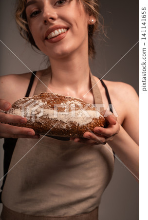 Woman baker holding fresh homemade sourdough bread, smiling and offering artisan loaf to client Woman baker holding fresh homemade sourdough bread, smiling and offering artisan loaf to client 141141658