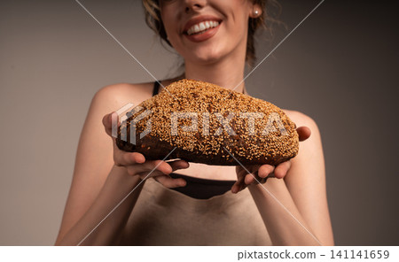 Baker woman holding fresh homemade whole grain bread with sesame seeds, showing healthy food and bakery concept Baker woman holding fresh homemade whole grain bread with sesame seeds, showing healthy food and bakery concept 141141659