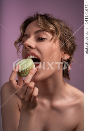 Young woman enjoying green macaron, savoring sweet dessert and indulgence on a vibrant purple background Young woman enjoying green macaron, savoring sweet dessert and indulgence on a vibrant purple background 141141675