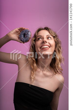 Young woman happily holding a blue frosted donut, excitedly looking up with space for text 141141700