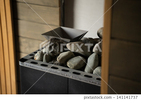 Sauna heater filling with natural stones and a small scoop, creating a relaxing wellness atmosphere Sauna heater filling with natural stones and a small scoop, creating a relaxing wellness atmosphere 141141737