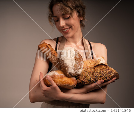 Young woman baker wearing apron presenting a variety of freshly baked rustic artisanal sourdough bread loaves Young woman baker wearing apron presenting a variety of freshly baked rustic artisanal sourdough bread loaves 141141846