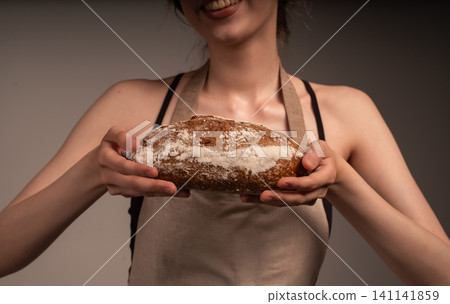 Baker holding fresh artisan bread with flour, smiling young woman showing healthy homemade loaf Baker holding fresh artisan bread with flour, smiling young woman showing healthy homemade loaf 141141859