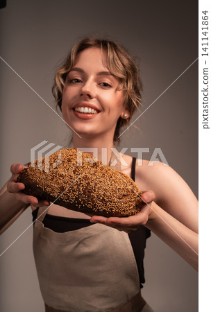 Smiling woman holding fresh baked seeded bread, representing artisan bakery, healthy eating, and homemade food Smiling woman holding fresh baked seeded bread, representing artisan bakery, healthy eating, and homemade food 141141864