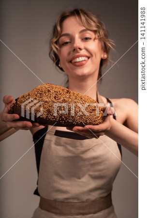 Smiling woman baker presenting a rustic, freshly baked whole grain sourdough bread loaf, sprinkled with sesame seeds Smiling woman baker presenting a rustic, freshly baked whole grain sourdough bread loaf, sprinkled with sesame seeds 141141988