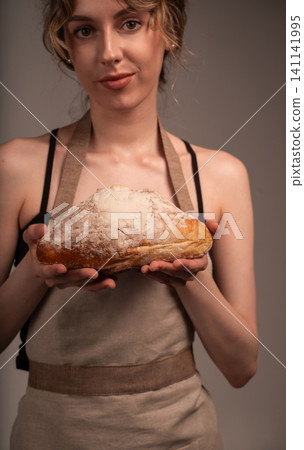 Woman baker wearing apron presenting fresh artisan sourdough bread loaf with flour dusted crust Woman baker wearing apron presenting fresh artisan sourdough bread loaf with flour dusted crust 141141995