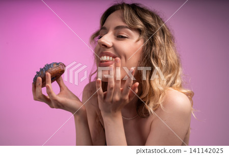 Young woman enjoying a donut, licking fingers, expressing sweet indulgence and happiness on a pink background Young woman enjoying a donut, licking fingers, expressing sweet indulgence and happiness on a pink background 141142025