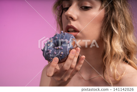 Woman enjoying a delicious purple glazed donut, biting into sweet dessert with sprinkles, indulging in a treat Woman enjoying a delicious purple glazed donut, biting into sweet dessert with sprinkles, indulging in a treat 141142026
