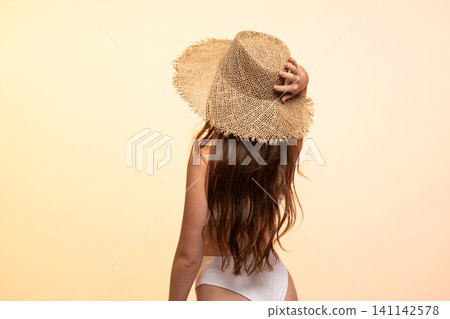 Woman with long hair wearing a wide-brimmed straw hat and white bikini bottom, relaxing on a warm summer holiday Woman with long hair wearing a wide-brimmed straw hat and white bikini bottom, relaxing on a warm summer holiday 141142578
