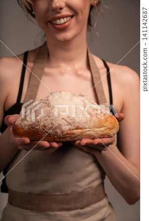 Woman baker holding a freshly baked, crusty sourdough bread loaf with flour dusting, smiling in an artisan apron 141142687