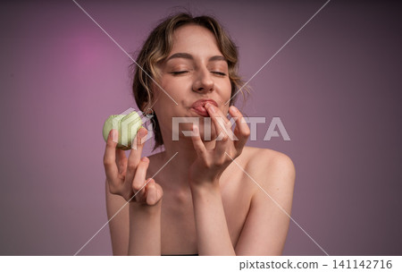Young woman enjoying sweet macaroon, closing eyes and licking fingers, experiencing pleasure and delicious taste Young woman enjoying sweet macaroon, closing eyes and licking fingers, experiencing pleasure and delicious taste 141142716