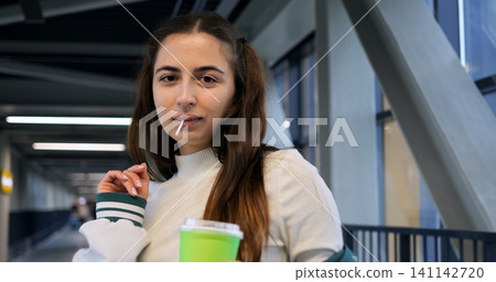 Woman with bright smile and friendly attitude. Portrait of joyful woman holding drink with inviting look. Lively woman smiling warmly while holding cup and gazing engagingly at camera Woman with bright smile and friendly attitude. Portrait of joyful woman holding drink with inviting look. Lively woman smiling warmly while holding cup and gazing engagingly at camera 141142720