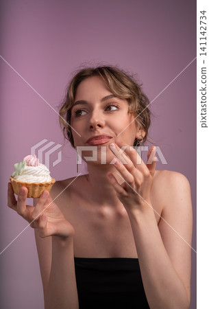 Young woman enjoying cream cupcake, looking away playfully, contemplating sweet dessert temptation and indulgence Young woman enjoying cream cupcake, looking away playfully, contemplating sweet dessert temptation and indulgence 141142734