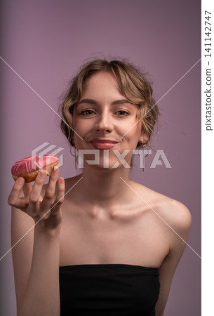 Young woman enjoying sweet pink donut, indulging in a moment of sugary pleasure and delicious dessert Young woman enjoying sweet pink donut, indulging in a moment of sugary pleasure and delicious dessert 141142747