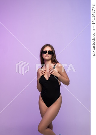 Woman posing in black swimsuit and sunglasses in studio with purple gradient background, embodying summer style and confidence Woman posing in black swimsuit and sunglasses in studio with purple gradient background, embodying summer style and confidence 141142778