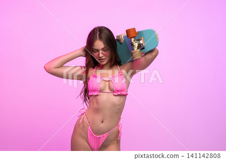 Young woman in pink bikini holding skateboard on shoulder, wearing sunglasses against vibrant neon background Young woman in pink bikini holding skateboard on shoulder, wearing sunglasses against vibrant neon background 141142808