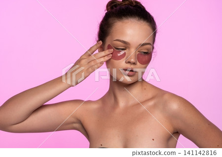 Young woman applying under eye patches for skin care routine, wellness and beauty treatment on pink background Young woman applying under eye patches for skin care routine, wellness and beauty treatment on pink background 141142816