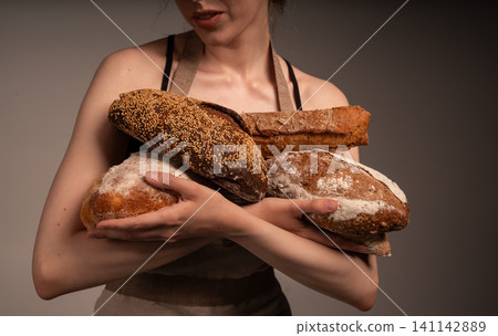 Woman baker holding rustic artisan loaves, presenting fresh organic and crusty homemade bread assortment Woman baker holding rustic artisan loaves, presenting fresh organic and crusty homemade bread assortment 141142889