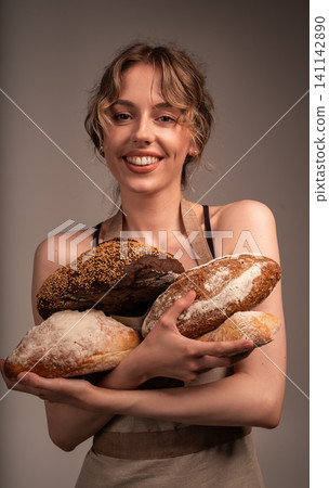 Smiling baker woman holding fresh artisanal baguettes and round loaves, offering delicious baked goods from a local bakery Smiling baker woman holding fresh artisanal baguettes and round loaves, offering delicious baked goods from a local bakery 141142890