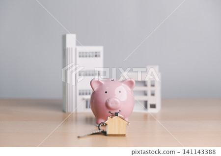 Pink piggy bank with house key and modern building models, symbolizing property ownership, real estate savings, mortgage deposit, home buying, and investment planning. 141143388