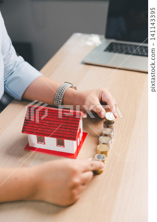 Property savings growth concept with hands stacking coins beside red house model, showing mortgage deposit, home budget, real estate investment, ownership planning, financial security, and wealth. Property savings growth concept with hands stacking coins beside red house model, showing mortgage deposit, home budget, real estate investment, ownership planning, financial security, and wealth. 141143395