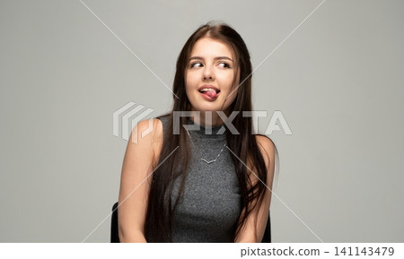 Young woman with humorous expression sticking out tongue and looking to the side on a light background Young woman with humorous expression sticking out tongue and looking to the side on a light background 141143479