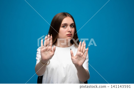 Young woman making a stop gesture, showing refusal, denial, and disagreement with a serious expression Young woman making a stop gesture, showing refusal, denial, and disagreement with a serious expression 141143591
