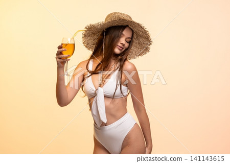 Woman posing in a studio for summer, wearing a swimsuit and hat, holding a drink and feeling relaxed Woman posing in a studio for summer, wearing a swimsuit and hat, holding a drink and feeling relaxed 141143615
