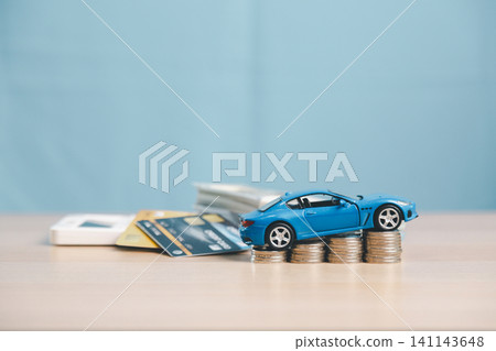 Blue toy car on coin stacks with credit card, calculator, and cash, symbolizing car finance, auto loan payment, vehicle purchase budget, and insurance cost. Blue toy car on coin stacks with credit card, calculator, and cash, symbolizing car finance, auto loan payment, vehicle purchase budget, and insurance cost. 141143648