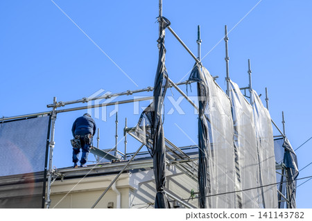 Craftsmen performing roof repair work on temporary scaffolding. Craftsmen performing roof repair work on temporary scaffolding. 141143782