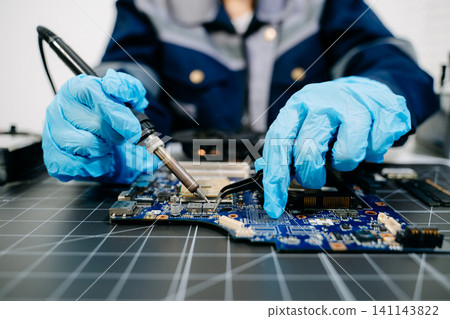 Closeup of expert soldering a green PCB board using precision tools. Ideal for electronics, circuit repair, engineering Closeup of expert soldering a green PCB board using precision tools. Ideal for electronics, circuit repair, engineering 141143822