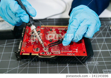 Professional technician repairing a graphics card PCB using soldering equipment. Ideal for technology, electronics repair, engineering and IT service concepts. Professional technician repairing a graphics card PCB using soldering equipment. Ideal for technology, electronics repair, engineering and IT service concepts. 141143896