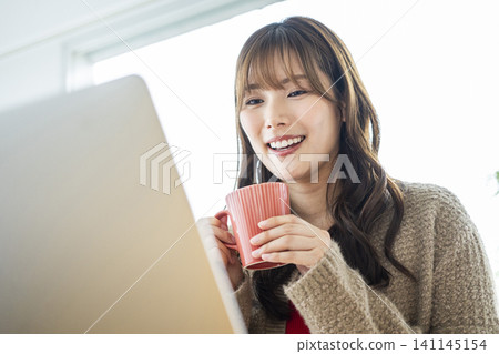 A young woman working on her laptop while drinking coffee. A young woman working on her laptop while drinking coffee. 141145154