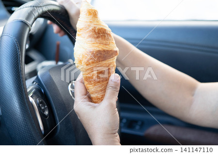 Bangkok, Thailand November 18, 2023 Asian woman driver hold and eat french fries in car, dangerous and risk an accident. 141147110