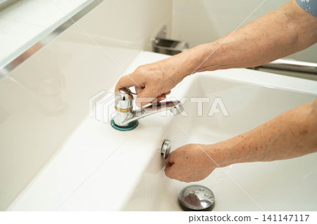 Asian elderly woman washing hands in bathroom. Asian elderly woman washing hands in bathroom. 141147117