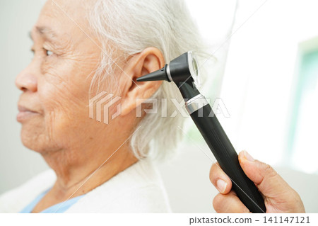 Otolaryngologist or ENT physician doctor examining senior patient ear with otoscope, hearing loss problem. 141147121