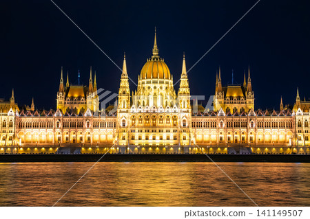 A fantastical night view of the Hungarian Parliament building reflected in the golden light on the surface of the Danube River in Budapest, Hungary. A fantastical night view of the Hungarian Parliament building reflected in the golden light on the surface of the Danube River in Budapest, Hungary. 141149507