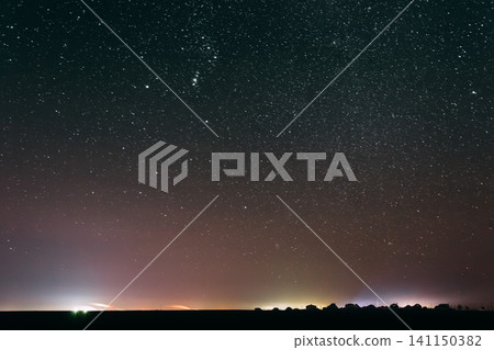 starry night sky over a dark horizon with distant city lights. starry night sky over a dark horizon with distant city lights. 141150382