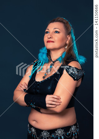 Woman performer in tribal fusion dance costume. Belly dancer with blue hair braid and ethnic accessory. Traditional artistic concept of oriental dance Woman performer in tribal fusion dance costume. Belly dancer with blue hair braid and ethnic accessory. Traditional artistic concept of oriental dance 141150666