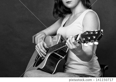 Young woman playing Spanish six string acoustic guitar in retro style. Monochrome photography with film grain and selective focus. Hobby, creativity and music education concept 141150717