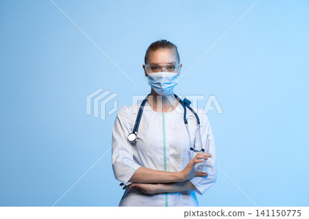Healthcare worker in uniform with stethoscope, wearing protective mask and glasses, holding syringe, focusing on treatment and health Healthcare worker in uniform with stethoscope, wearing protective mask and glasses, holding syringe, focusing on treatment and health 141150775