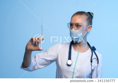 Doctor or nurse in medical mask and safety glasses holding a syringe with vaccine, preparing for injection Doctor or nurse in medical mask and safety glasses holding a syringe with vaccine, preparing for injection 141150777