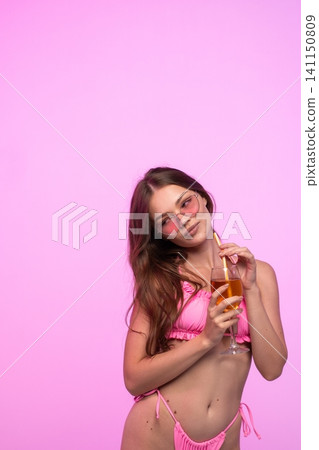 Stylish young woman in pink bikini and sunglasses sipping refreshing drink against bright pink background Stylish young woman in pink bikini and sunglasses sipping refreshing drink against bright pink background 141150809