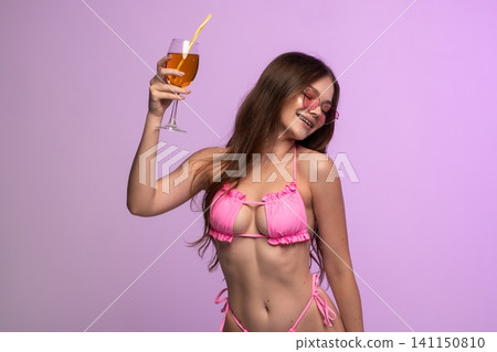Young woman in pink bikini celebrating summer vacation, holding a refreshing cocktail with heart-shaped sunglasses, smiling Young woman in pink bikini celebrating summer vacation, holding a refreshing cocktail with heart-shaped sunglasses, smiling 141150810