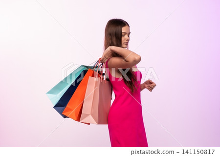 Woman in a pink dress holding several vibrant shopping bags, representing consumerism, fashion, and lifestyle 141150817