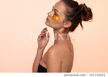 Woman applying golden eye patches, enjoying a revitalizing skin care routine for beauty and under eye treatment Woman applying golden eye patches, enjoying a revitalizing skin care routine for beauty and under eye treatment 141150825