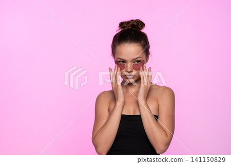 Woman applying under eye patches for skincare, promoting beauty and self care on a pink background 141150829