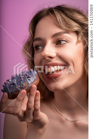 Woman enjoying a sweet donut with purple icing, smiling happily and feeling the temptation of dessert Woman enjoying a sweet donut with purple icing, smiling happily and feeling the temptation of dessert 141150869