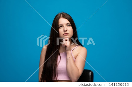 Woman in pink top looking up with a thoughtful expression, contemplating and questioning against a vibrant blue studio backdrop Woman in pink top looking up with a thoughtful expression, contemplating and questioning against a vibrant blue studio backdrop 141150913